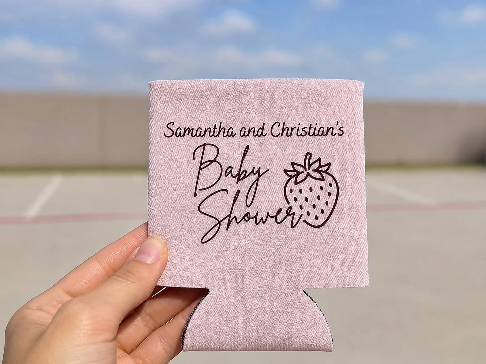 Pink baby shower koozie held outdoors against a cloudy sky