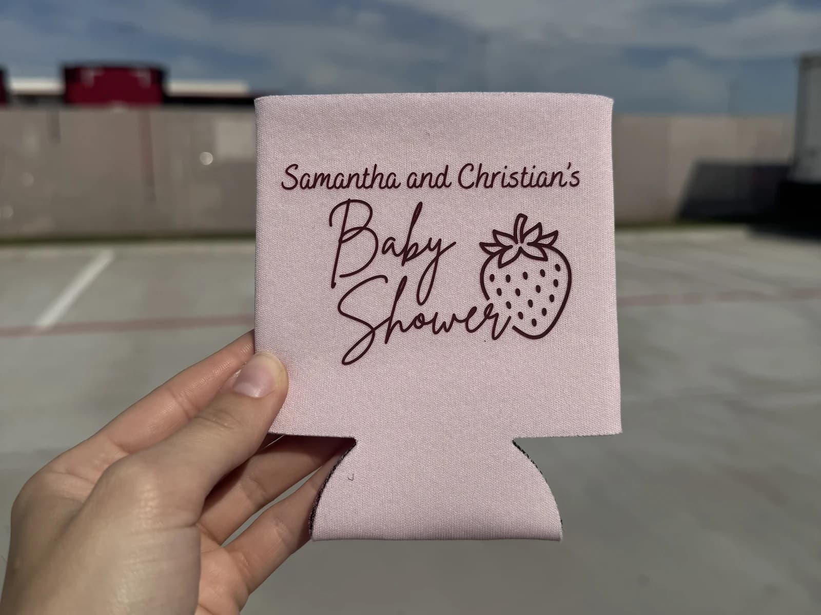 Pink custom baby shower koozie held outdoors