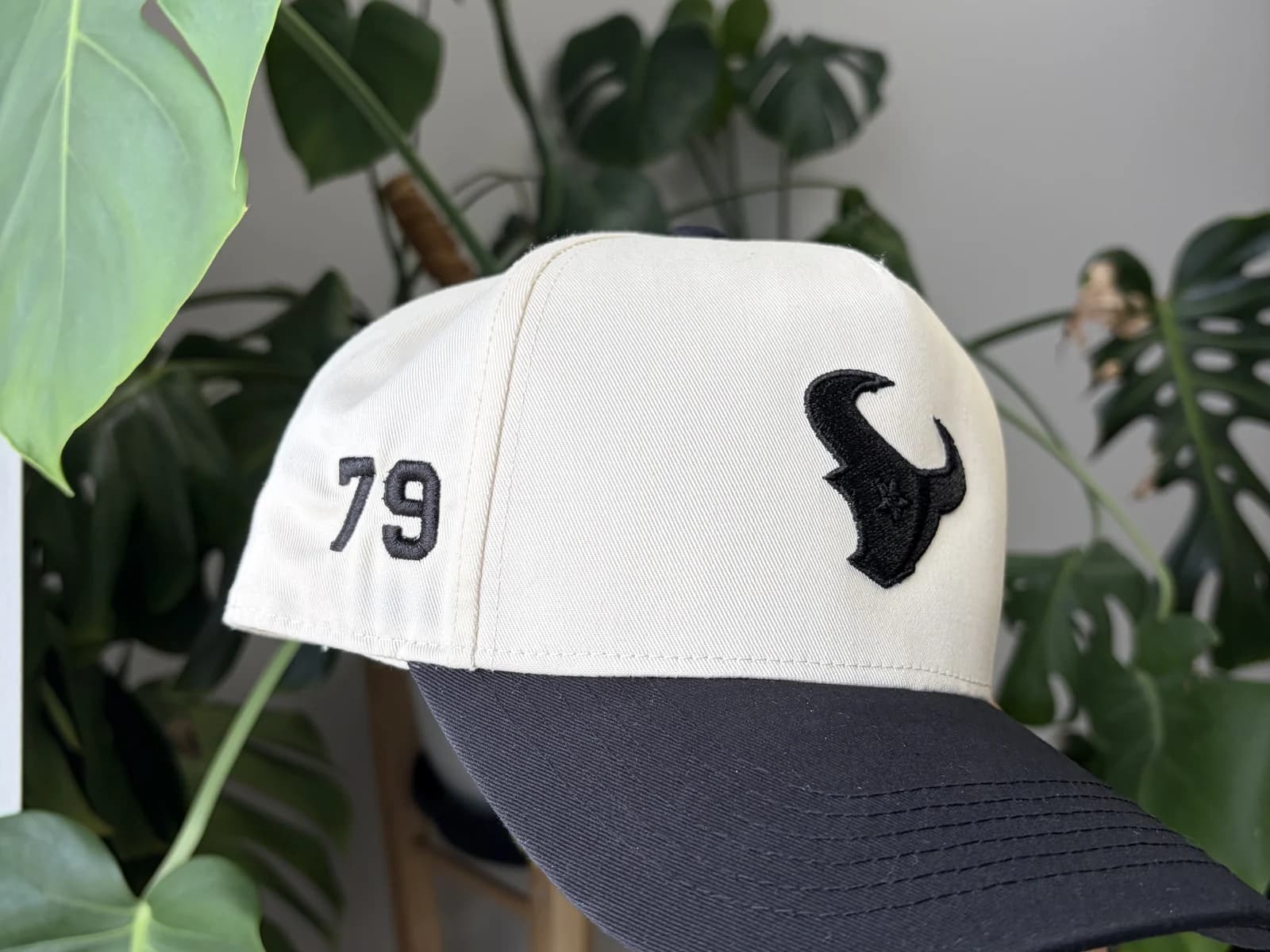 Cream and black custom embroidered hat displayed among plants